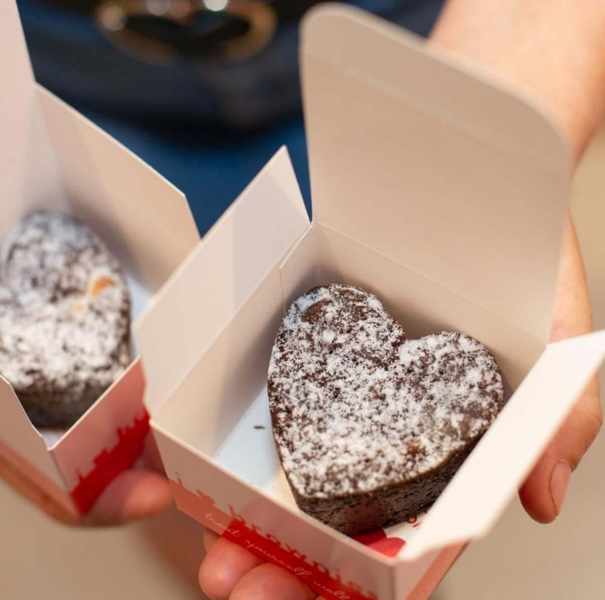 Heart-shaped chocolate brownie in a small box held by hands.