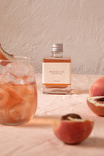 Cocktail bottle with peaches and a glass of peachy drink.