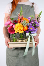Person holding a wooden crate with colorful flowers and plants.