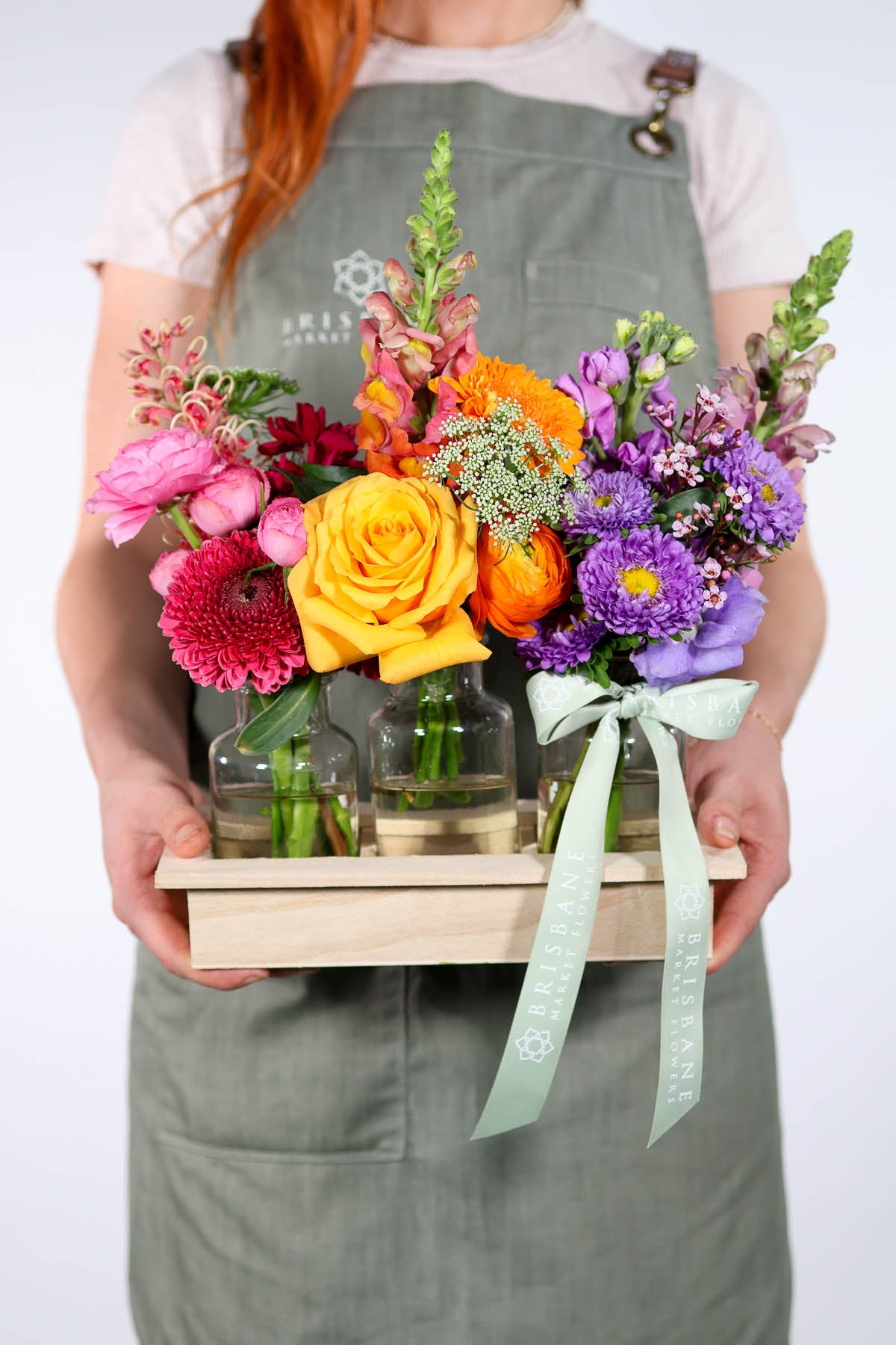 Person holding a wooden crate with colorful flowers and plants.