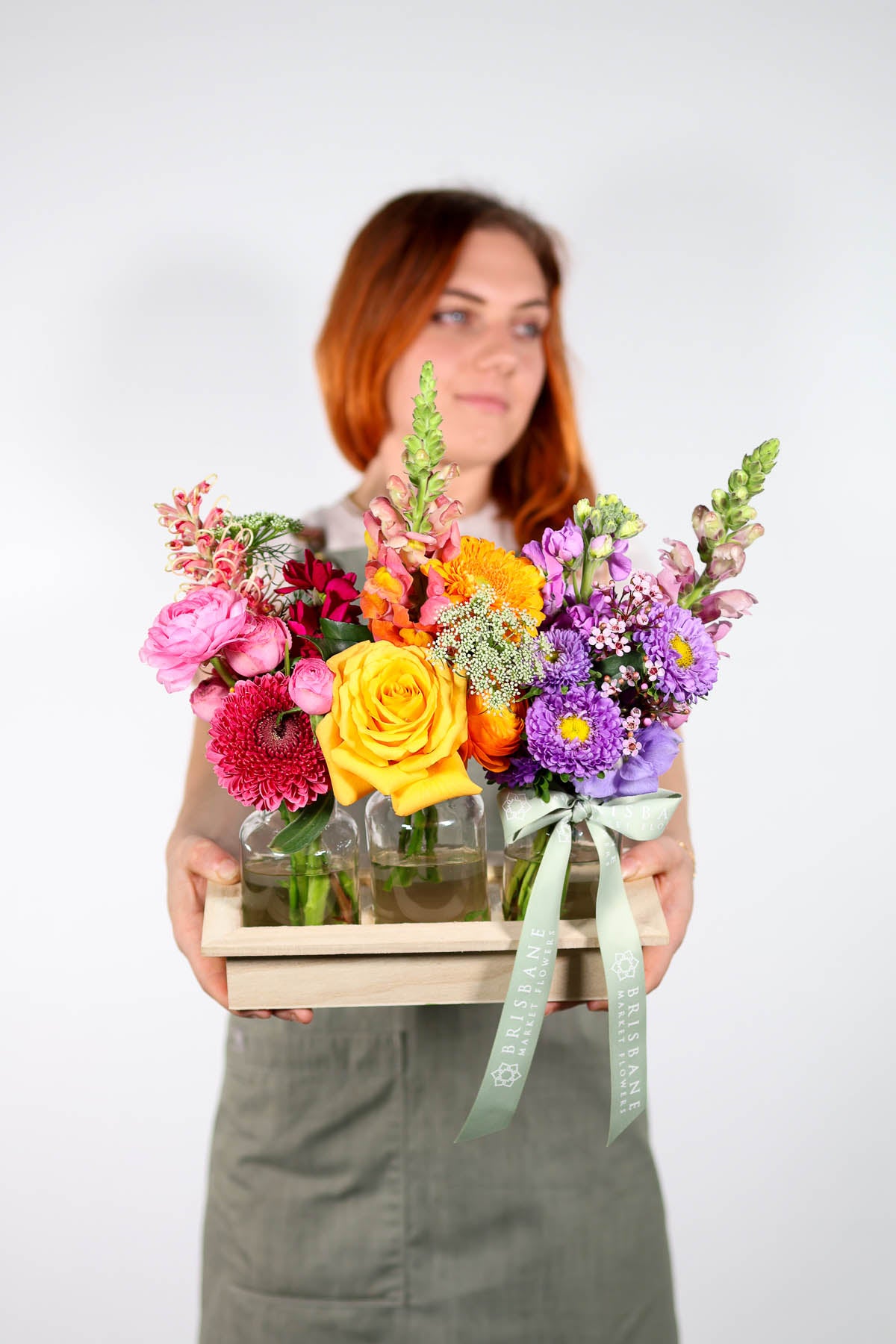 Woman holding a wooden crate of colorful flowers against a white background