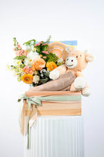 Floral arrangement with a plush toy ,baby wrap and indigenous baby book on a white background