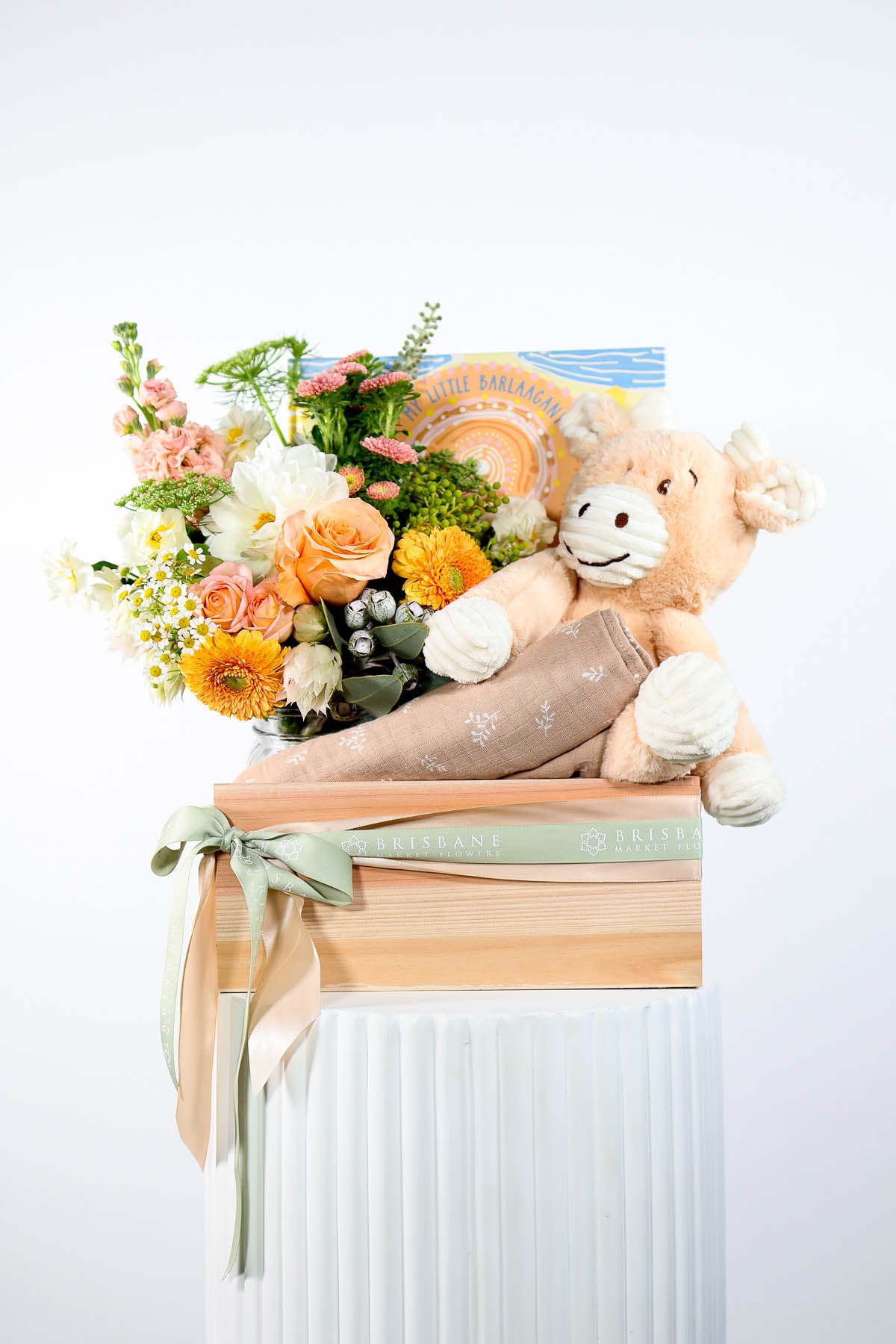 Floral arrangement with a plush toy ,baby wrap and indigenous baby book on a white background