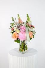 Bouquet of flowers in a glass vase on a white pedestal against a white background