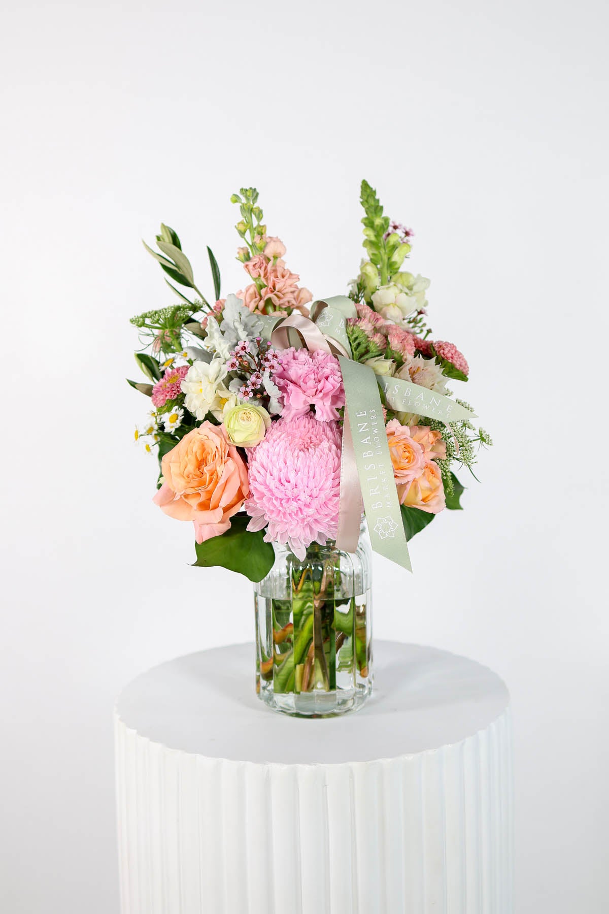 Bouquet of flowers in a glass vase on a white pedestal against a white background