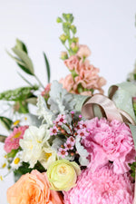 Bouquet of pastel flowers with pink and green ribbons on a light background