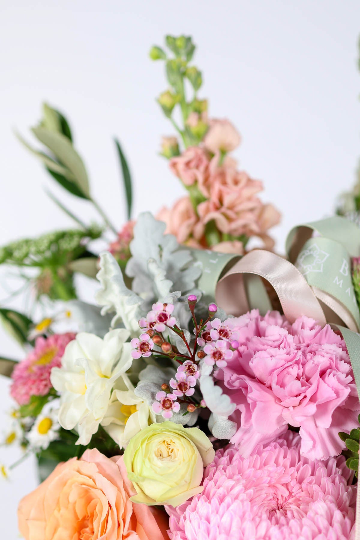 Bouquet of pastel flowers with pink and green ribbons on a light background