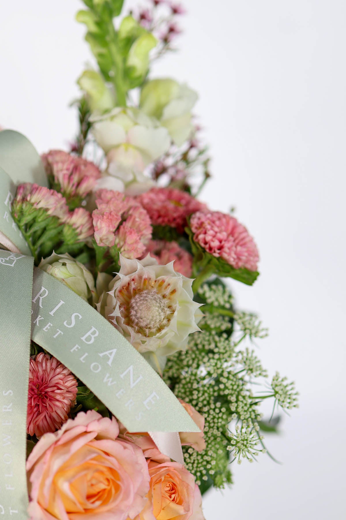 Vase of seasonal flowers with a green Brisbane Market Flowers ribbon on a white background