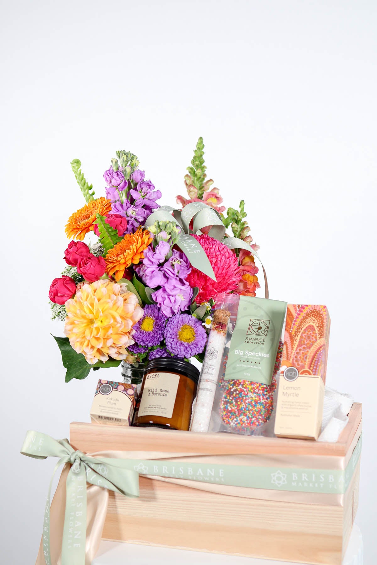 Gift hamper with flowers, chocolates, candle, and hand cream in a timber box.