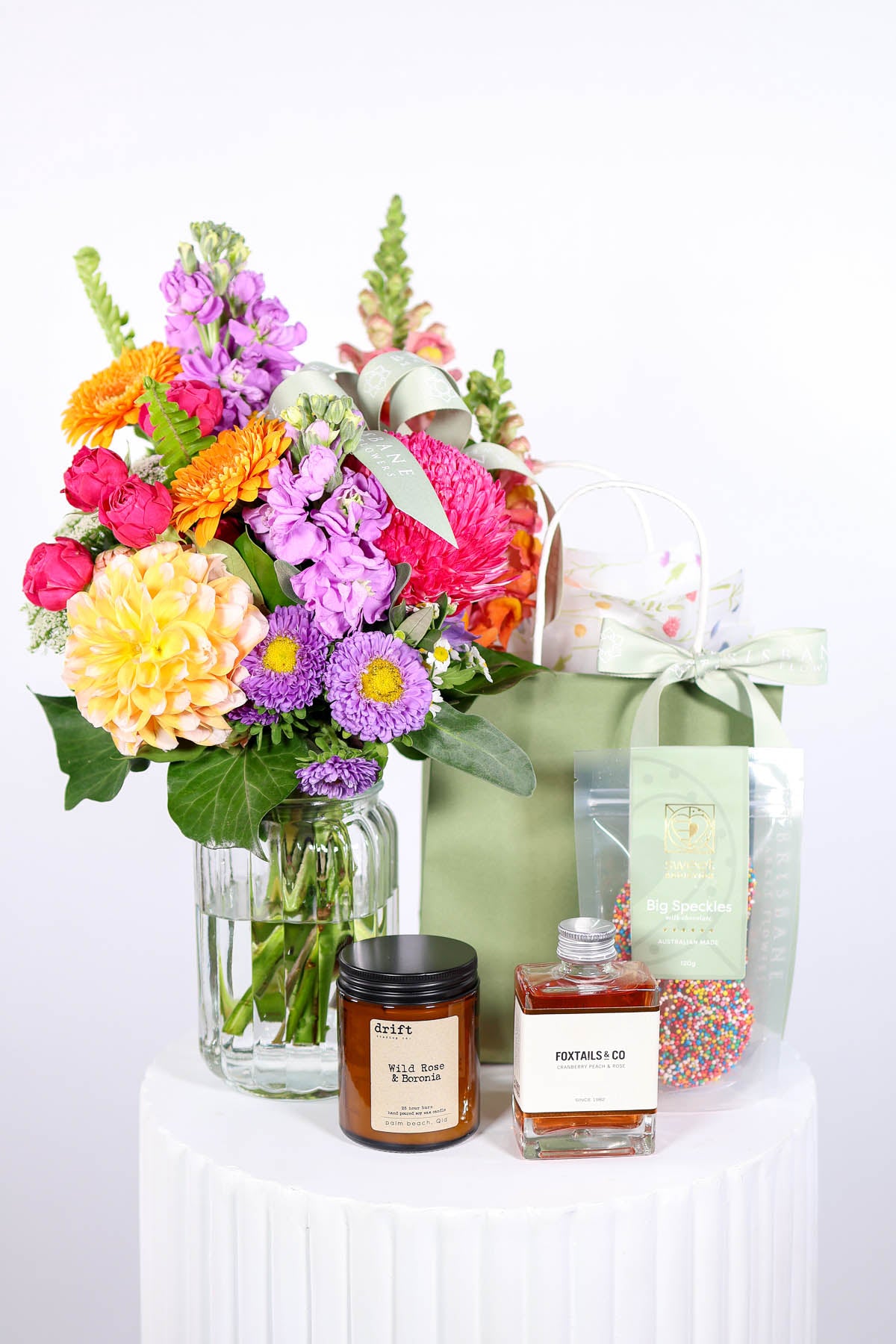 Bouquet of flowers, candles, and a gift bag on a white surface
