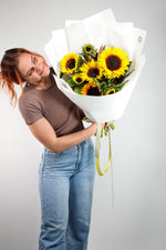 Person holding a bouquet of sunflowers against a plain background.