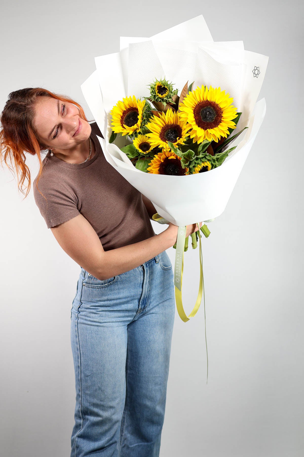 Person holding a bouquet of sunflowers against a plain background.