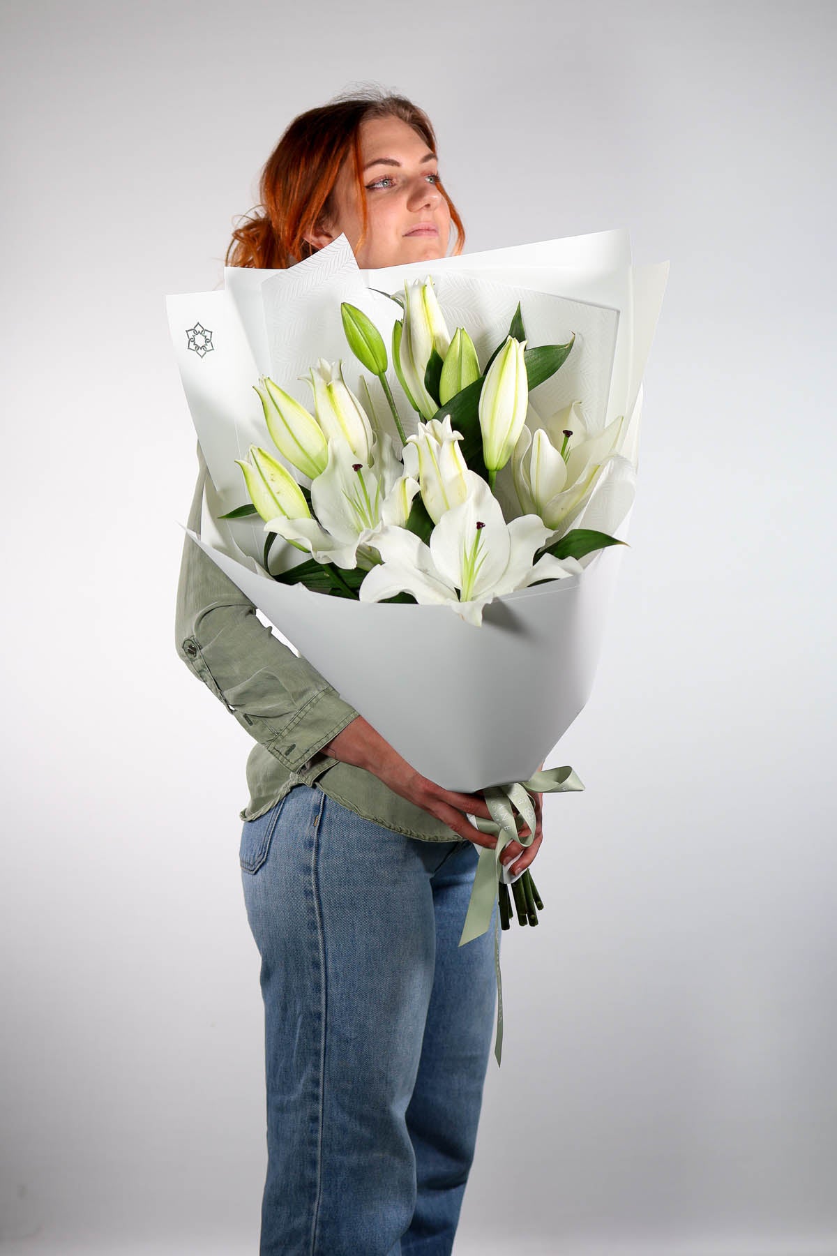 Person holding a large bouquet of white lilies against a plain background