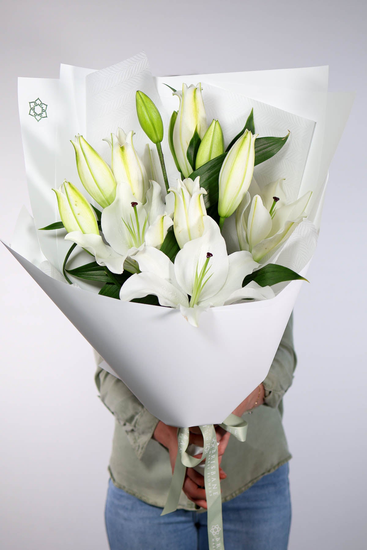 Bouquet of white lilies wrapped in paper held by a person against a light gray background