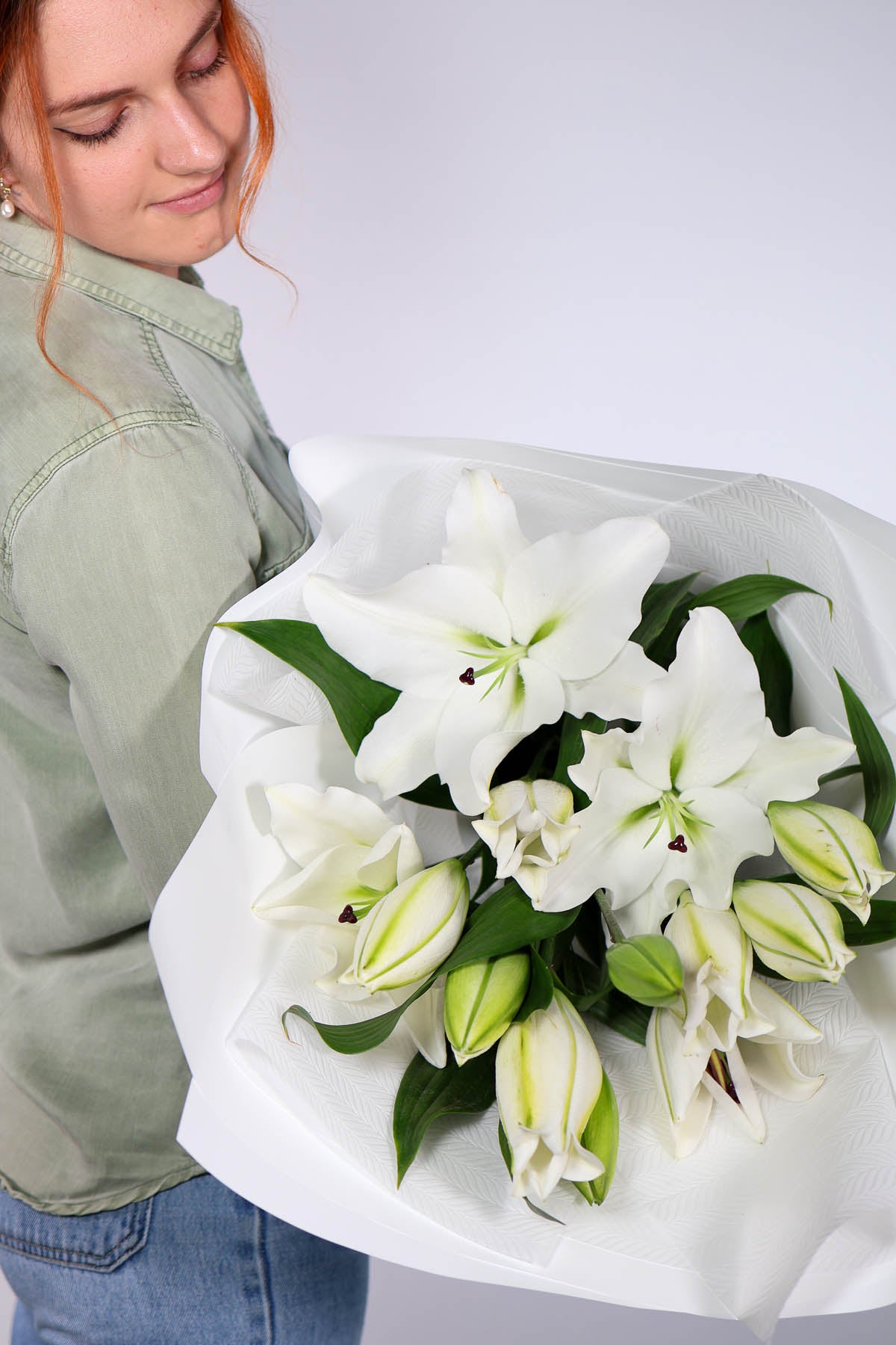 Florist holding a bouquet of lilies wrapped in white luxe paper.