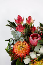 Side angle of hat box arrangement filled with proteas, banksias, and gum leaves for luxury Brisbane flower delivery