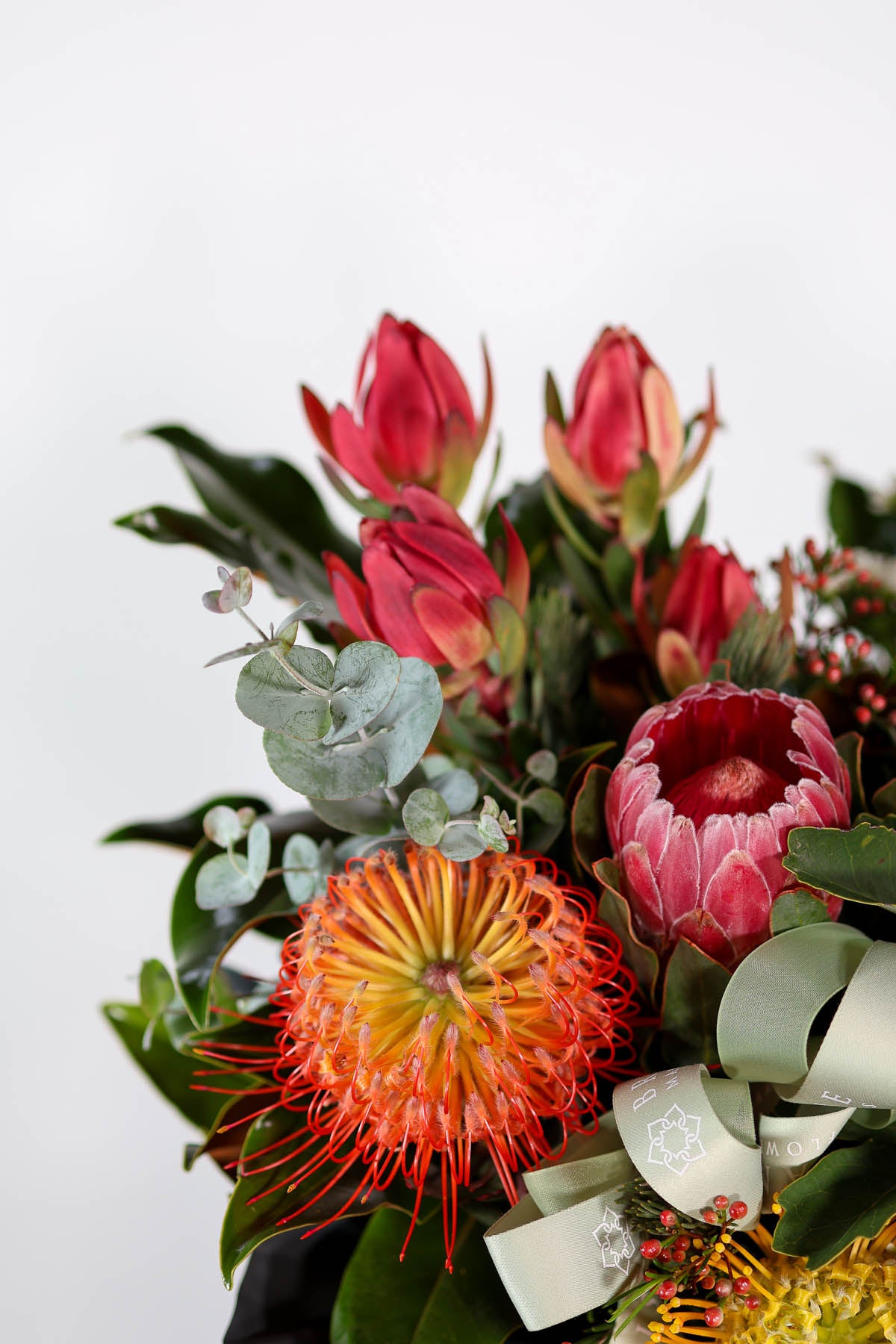 Side angle of hat box arrangement filled with proteas, banksias, and gum leaves for luxury Brisbane flower delivery