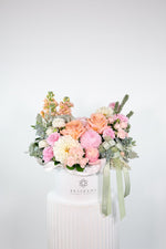Front-facing Milan floral design in white hatbox with pink, peach, and ivory seasonal blooms and eucalyptus foliage