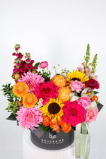 Colourful flower arrangement with sunflowers and pink and ornage flowers in a Brisbane Market Flowers box on a white background