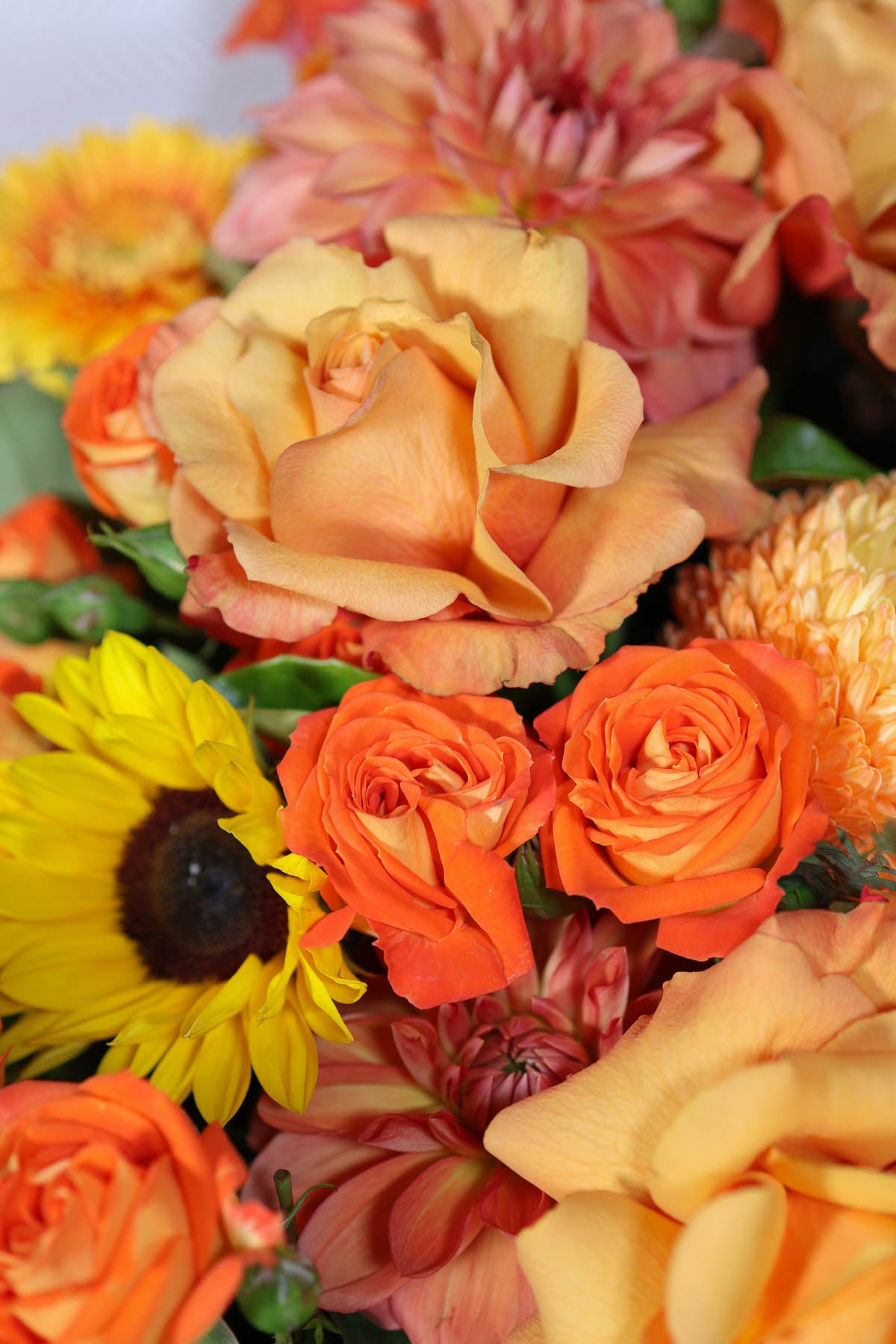Bouquet of colourful orange and yellow flowers including roses and sunflowers.