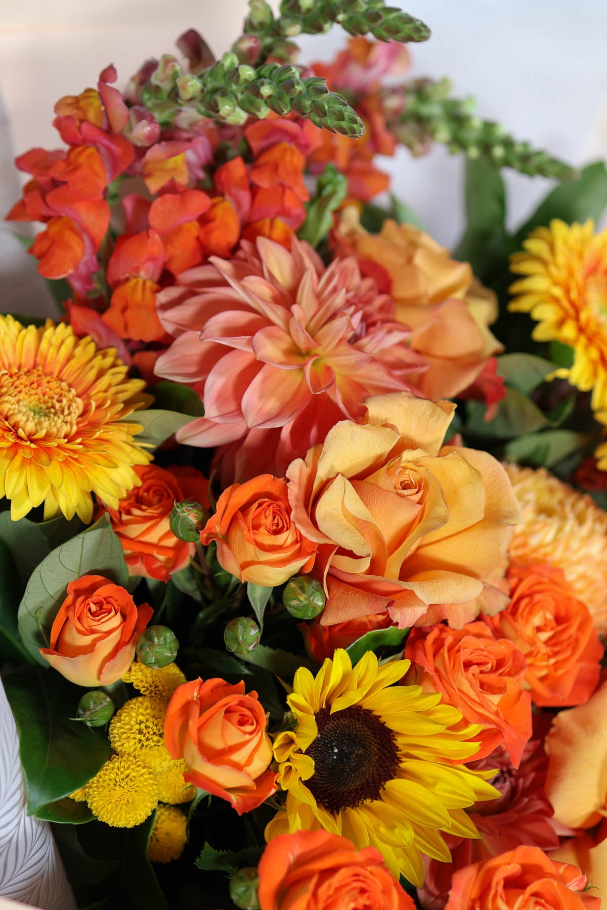 Bouquet of warm and bright orange and yellow flowers including roses, dahlia and sunflowers.