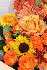 Bouquet of orange, yellow flowers including roses and sunflowers.