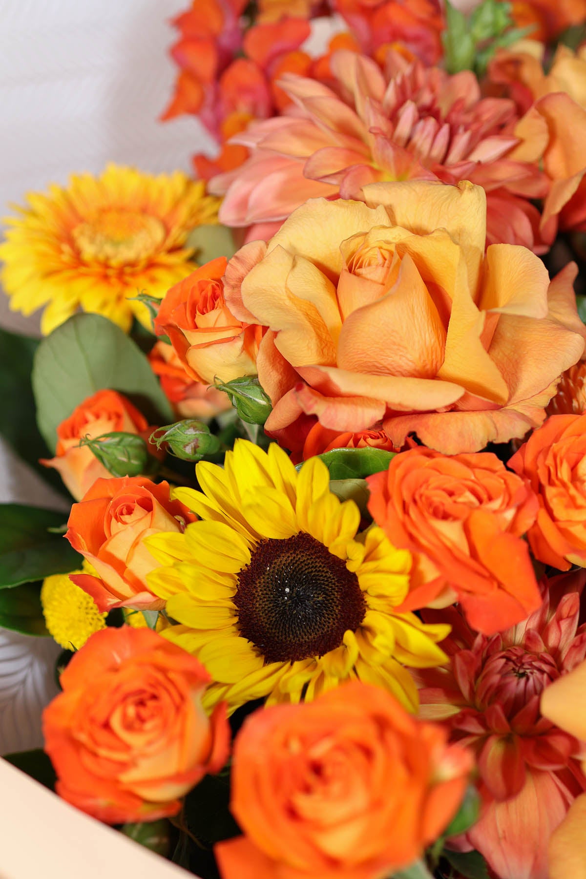 Bouquet of orange, yellow flowers including roses and sunflowers.