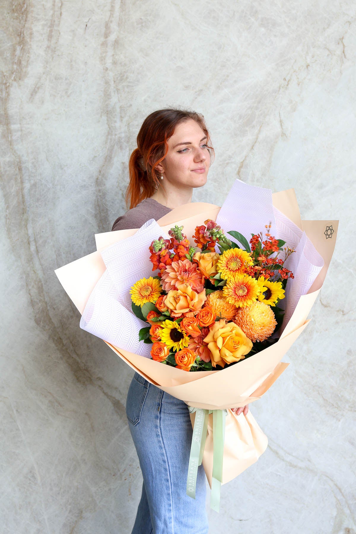 Woman holding a Premium floral design hand-tied autumn bouquet wrapped in white paper against a marble wall