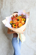 Person holding a Luxury autumn bouquet Brisbane – orange, gold and rust flowers in premium wrap
