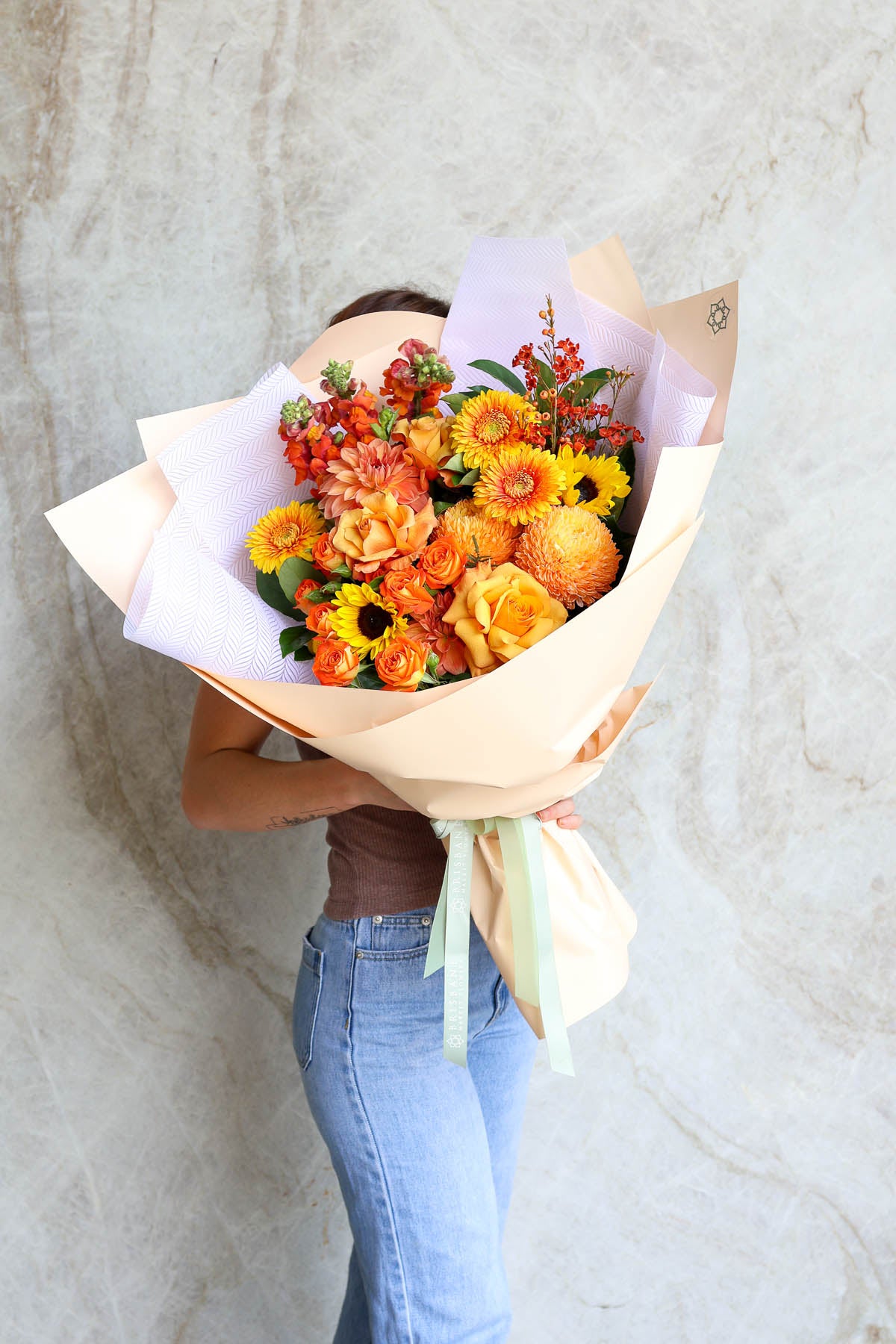Person holding a Luxury autumn bouquet Brisbane – orange, gold and rust flowers in premium wrap