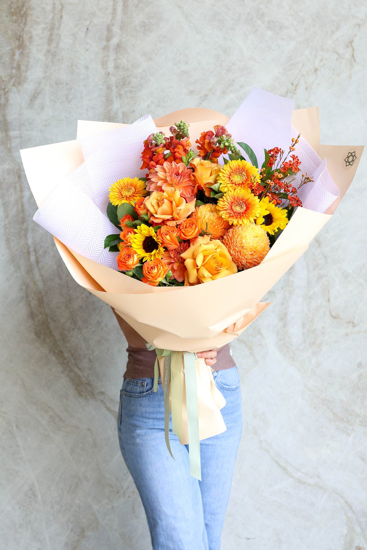 Bouquet of vibrant orange luxury flowers held by a person wearing light blue jeans against a neutral background
