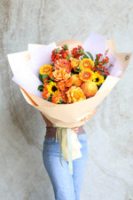 Bouquet of vibrant orange luxury flowers held by a person wearing light blue jeans against a neutral background