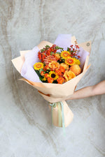 Arm holding luxury gift bouquet – seasonal flowers in orange, yellow and bronze tones Brisbane