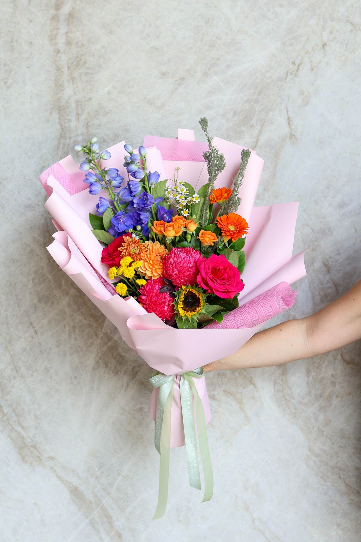 Model holding colourful summer bouquet showing bright flowers in hand-tied wrap for graduation gifting