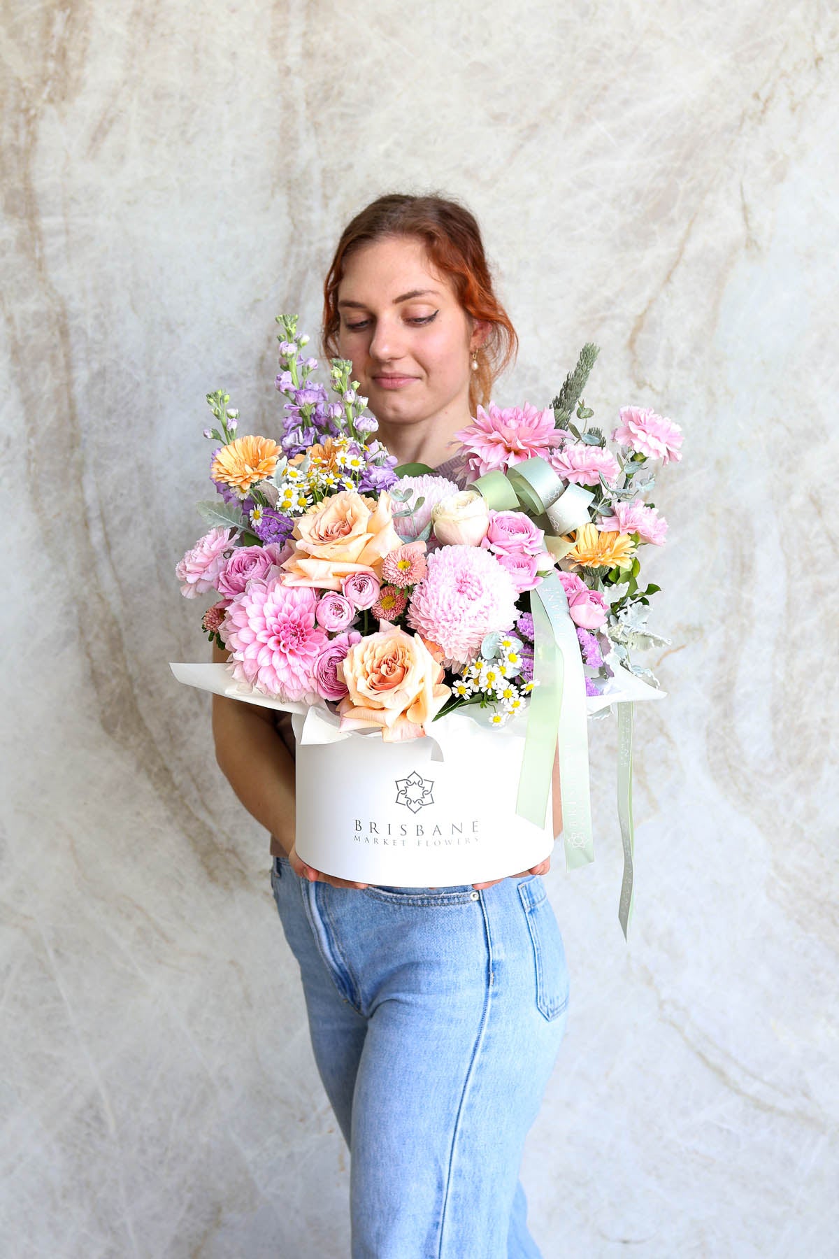 Woman holding a box of pastel and soft flowers against a marble background