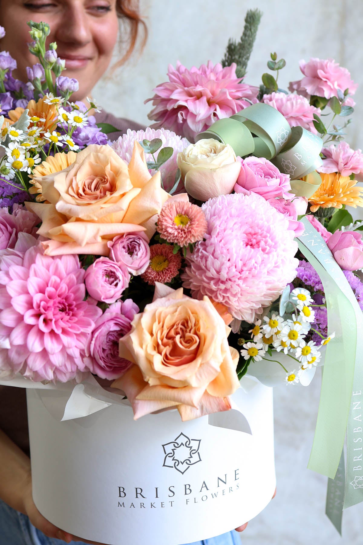 Pastel flower arrangment featuring roses and dahlia in a white hatbox with 'Brisbane Market Flowers' branding