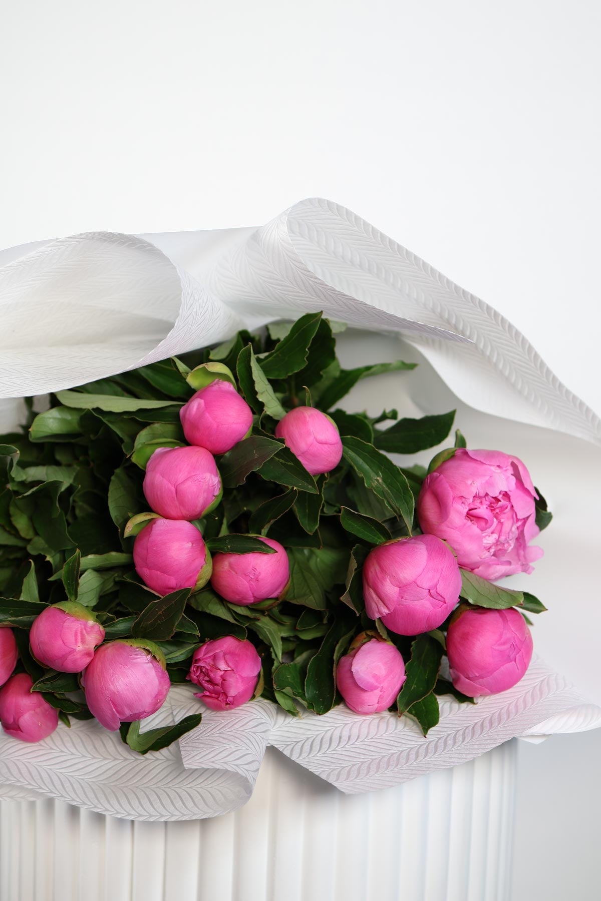 Bouquet of pink flowers wrapped in white paper on a white background