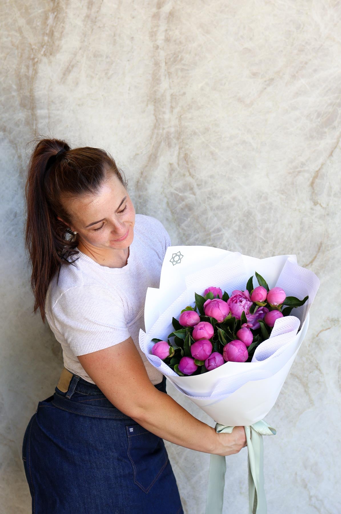 Person holding a bouquet of pink flowers against a marble wall.
