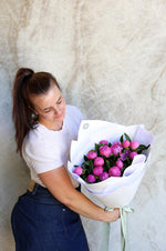 Person holding a bouquet of pink flowers against a marble wall.