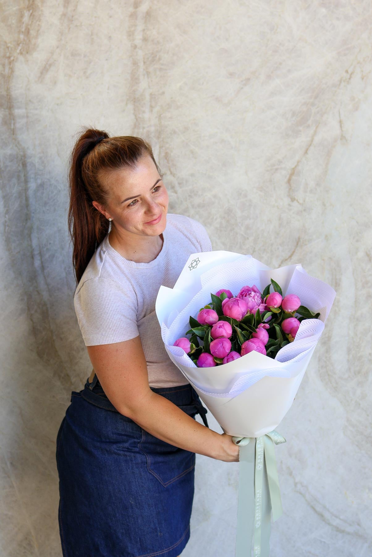 Person holding a bouquet of pink flowers against a marble background.