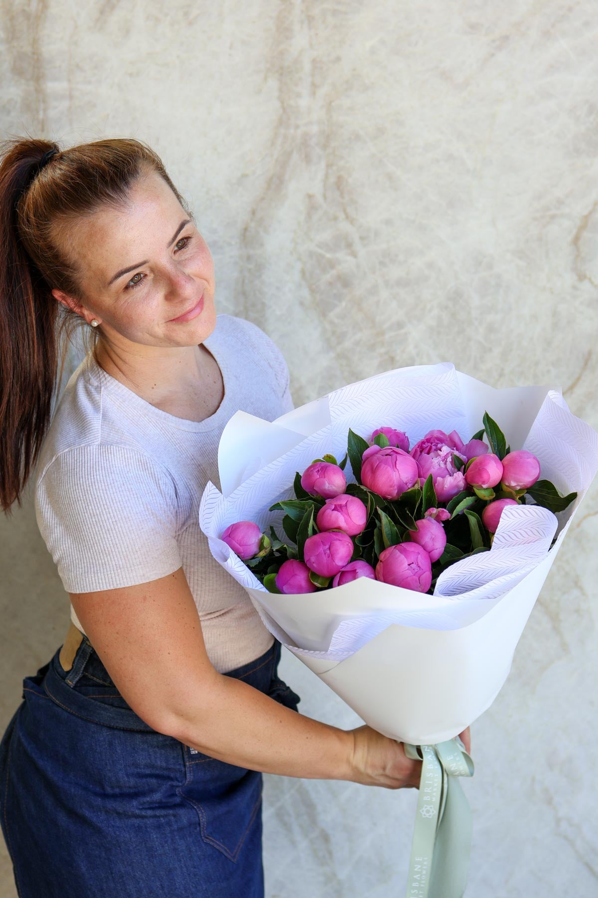 Woman holding a bouquet of pink flowers against a neutral background