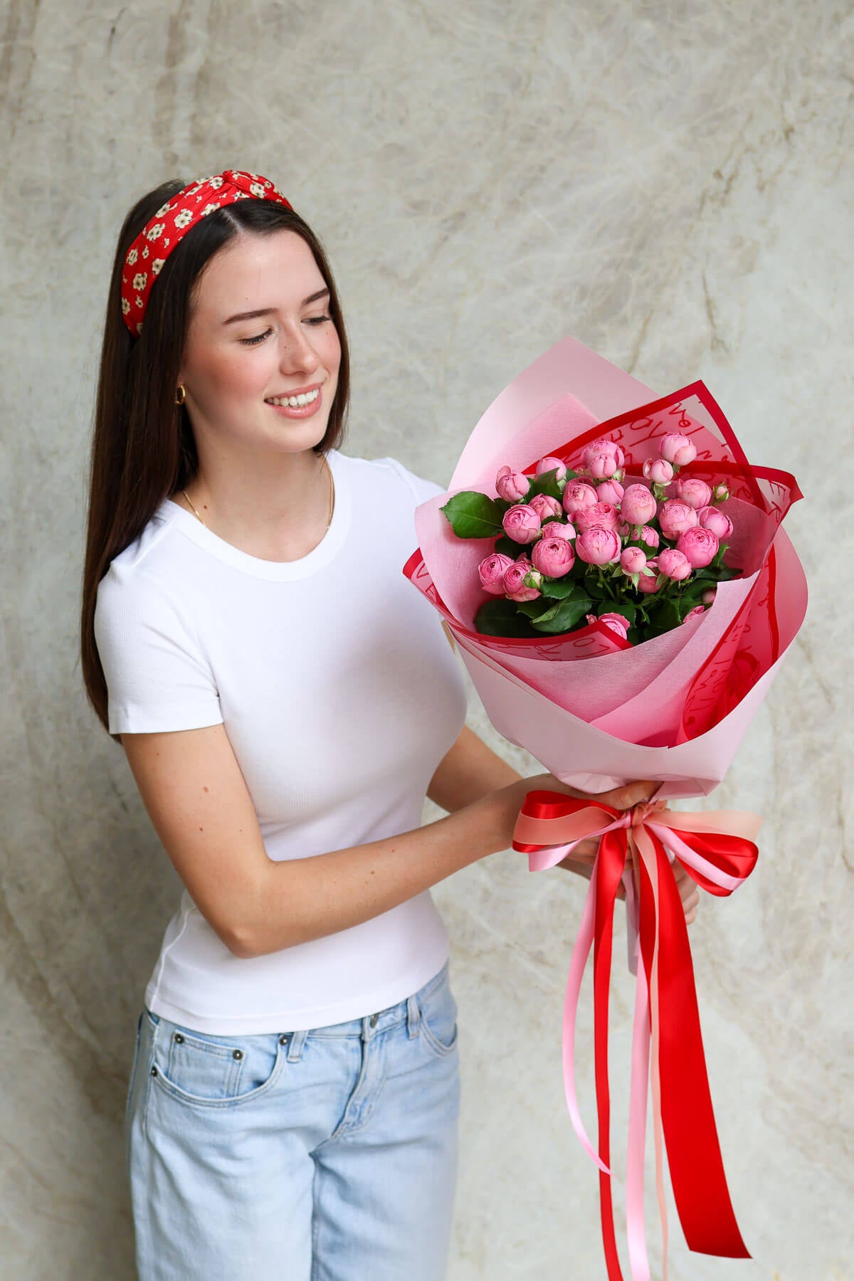 Woman holding a bouquet of pink roses  wrapped in Valentine's Day print with a red ribbon.