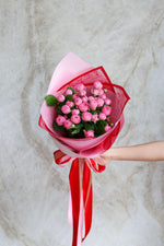 Bouquet of pink flowers wrapped in red paper with a ribbon against a marble background.