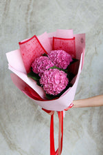 Bouquet of pink hydrangea wrapped in red and pink paper with a ribbon.