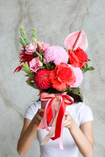 Person holding a pink vase of flowers with red reflexed roses and ribon detailing.