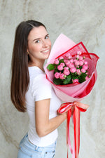 Woman holding a bouquet of pink flowers wrapped in Valentine's print.