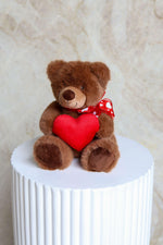 Brown teddy bear with a red heart and bow tie.