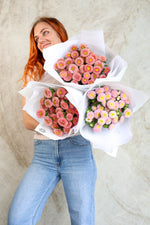 Woman holding three bouquets of pink and yellow aster flowers against a neutral marble background