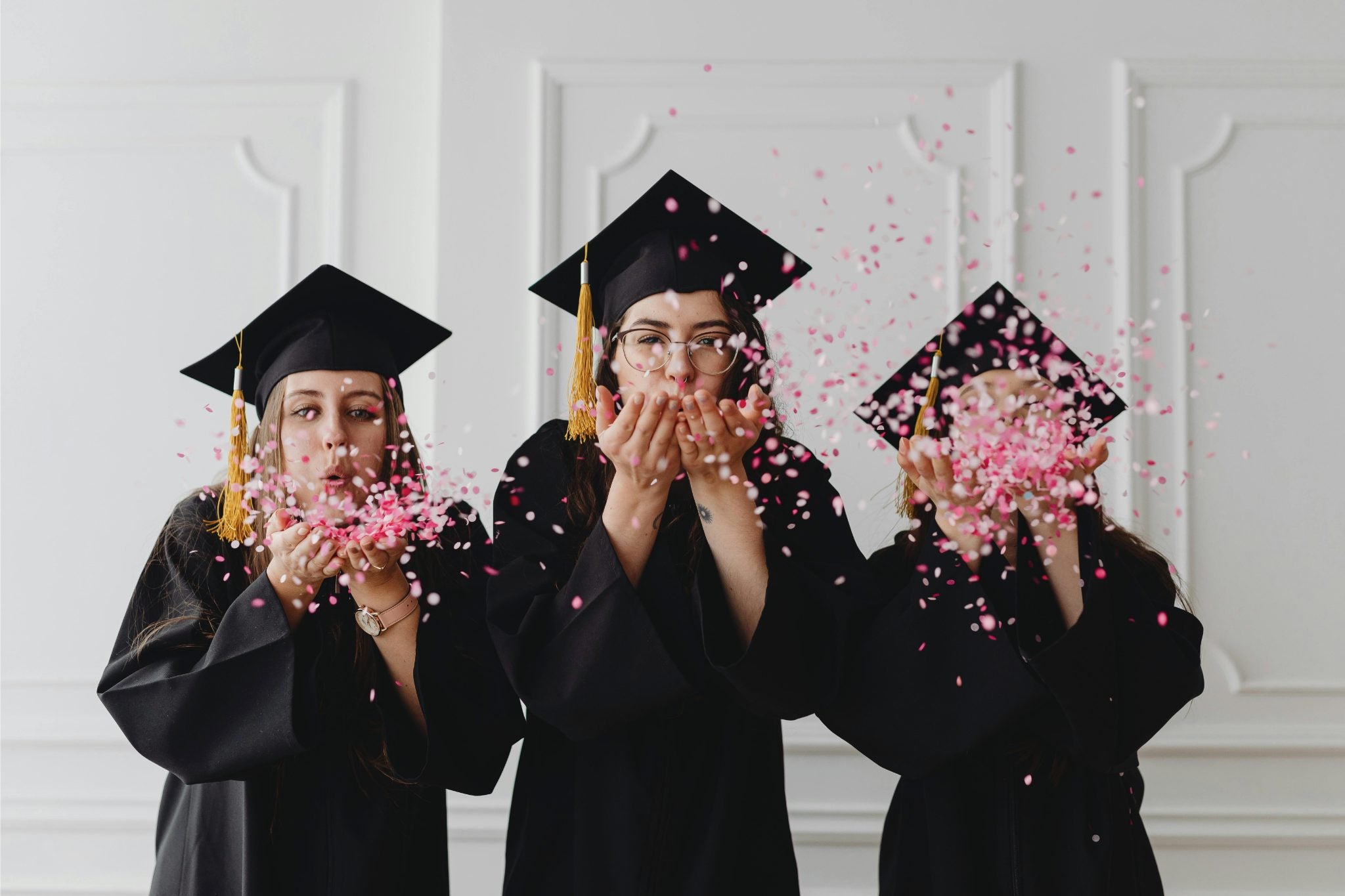 Three graduates in caps and gowns blowing confetti in Brisbane.