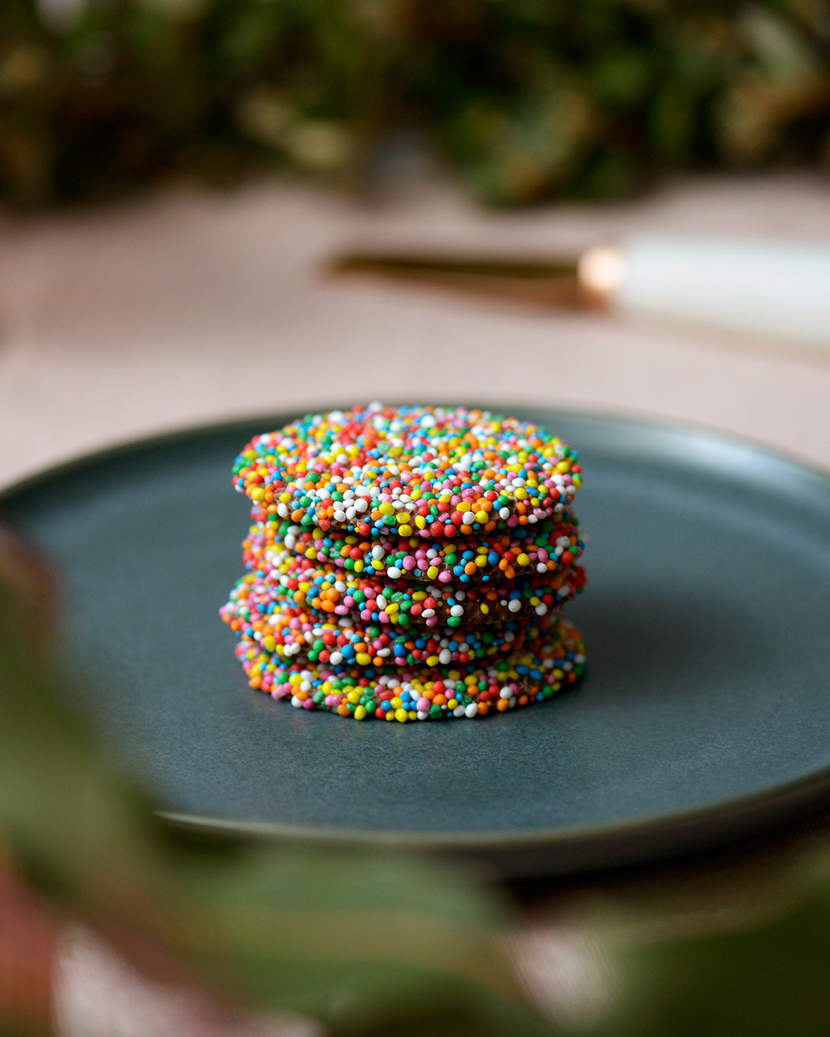 Delicious and colourful freckle chocolates stacked one on top of the other on a rustic blue plate.